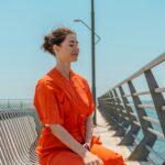 Woman in orange dress meditating by the ocean